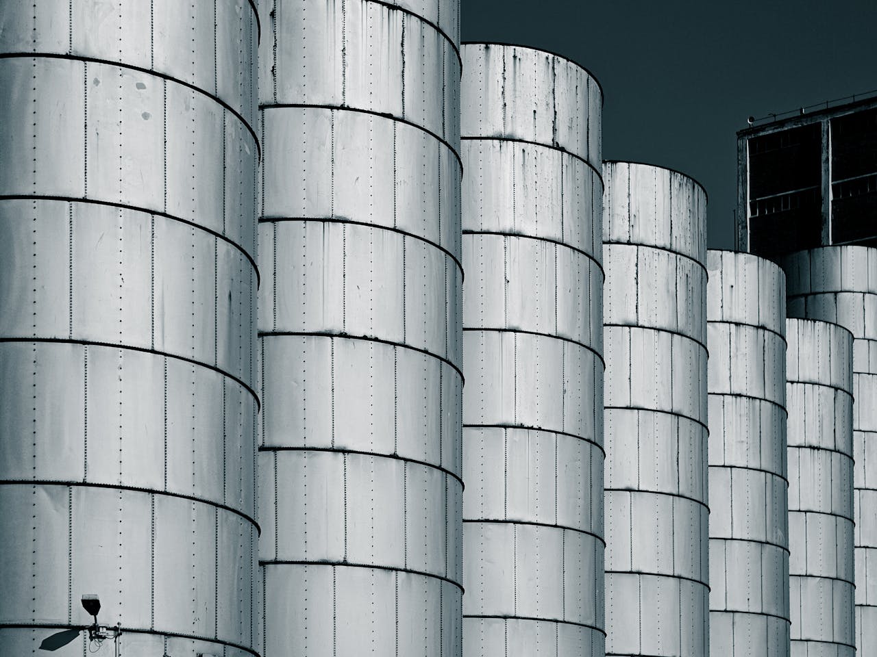 Close-up of industrial metal silos lined up against a dark blue sky, showcasing symmetry.
